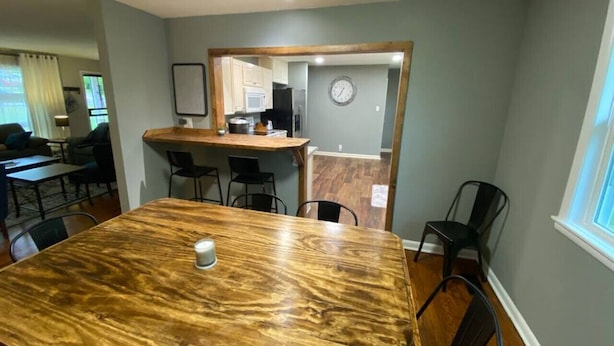 Un comedor con una mesa y sillas de madera, una cocina al fondo y un reloj en la pared.