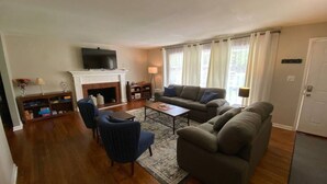 Una sala de estar con chimenea, televisor, sofá, mesa de centro y estantería.