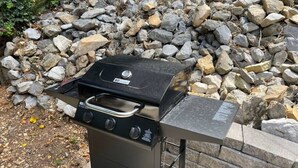 Un barbecue portatif doté de quatre brûleurs et d’un écran numérique, placé devant un mur de pierres et un tas de rochers.