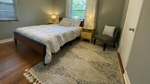 Une chambre à coucher comprenant un lit, des tables de chevet, une chaise, une fenêtre avec des rideaux et un ventilateur de plafond.