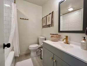 Un baño con inodoro blanco, lavabo con grifo dorado, espejo y cortina de ducha.