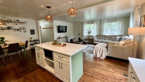 Een moderne keuken met witte kasten, een eethoek met een houten tafel en stoelen, en een woonkamer met een bank en een televisie.