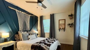 Een slaapkamer met een bed, nachtkastje, plafondventilator en een raam met gordijnen.