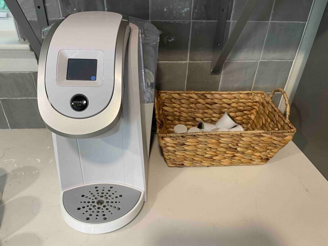 A coffee machine with a digital display and a control panel, next to a woven basket containing cups and a small container.