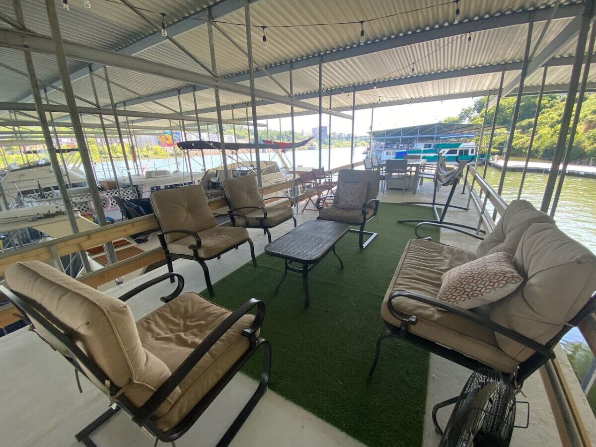 Een overdekt terras met stoelen en tafels, met uitzicht op een waterpartij met boten.