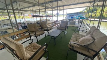 Een overdekt terras met stoelen en tafels, met uitzicht op een waterpartij met boten.