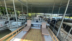 Une terrasse extérieure couverte, aménagée avec des sièges, un tapis à motifs et des bateaux en arrière-plan.