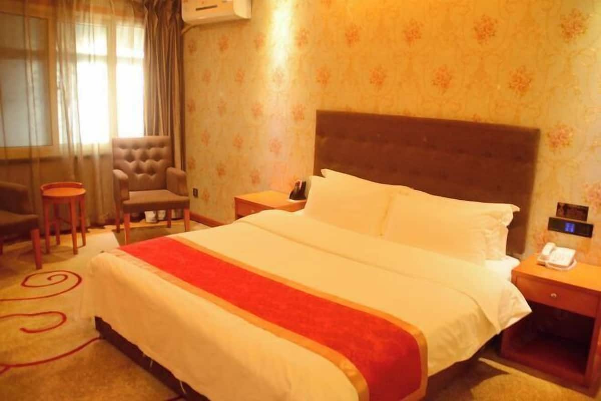 A hotel room with a large bed, a chair, a small table, and a nightstand with a phone.