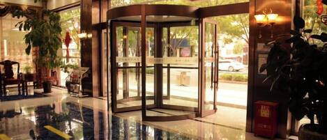 Un vestíbulo de hotel con puerta giratoria, piso de mármol pulido y plantas en macetas.