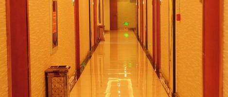A hotel corridor with a polished floor, doors on both sides, and a green exit sign at the end.