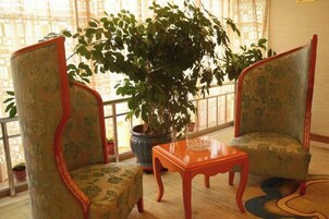 A room with two patterned armchairs, a wooden table, and a large potted plant.