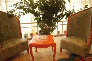 A room with two patterned chairs, a wooden table, and a large potted plant. - Dingxi Jingu Hotel (Dingxi)