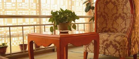 A balcony with a wooden table, a potted plant, and a patterned armchair.