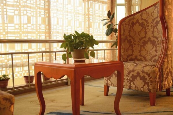 A balcony with a wooden table, a potted plant, and a patterned armchair.