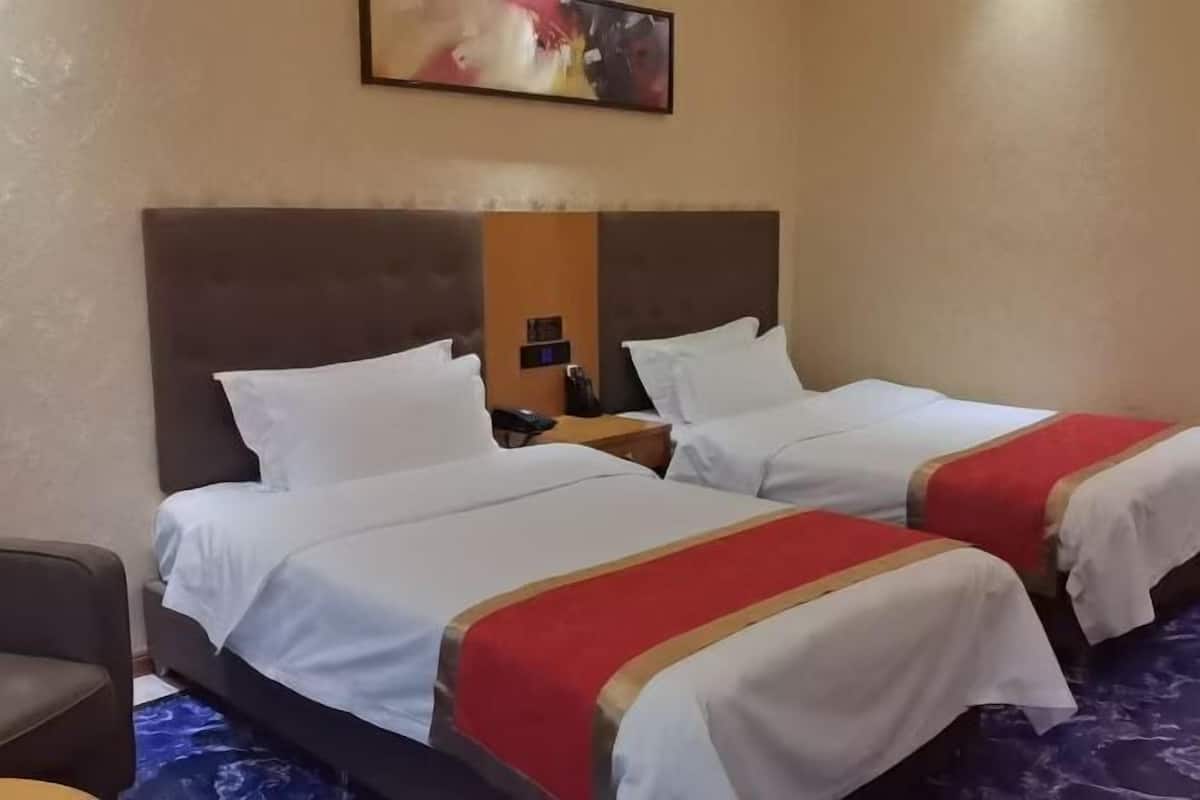 A hotel room with two beds, a nightstand, a chair, and a painting on the wall.