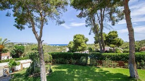 Un jardin bien entretenu, agrémenté de divers arbres et arbustes, une haie taillée avec soin et une vue dégagée sur la mer en arrière-plan.