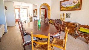 Une salle à manger avec une grande table en bois, plusieurs chaises, un lustre et un tableau accroché au mur.