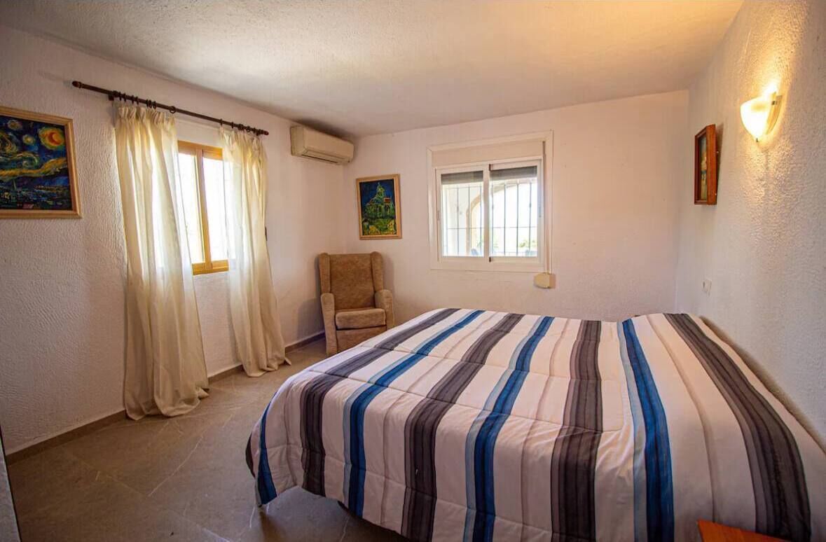 A bedroom with a bed, a chair, a window, and a painting on the wall.