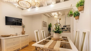 A dining area with a glass-top table, white chairs, a woven bench, and hanging plants.
