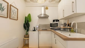 A compact kitchen with white cabinets, a stainless steel range hood, a microwave, and a sink. There's a small refrigerator and a potted plant on a side table.