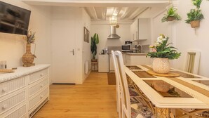A modern kitchen with white cabinets, a dining table with a glass top, and hanging plants.