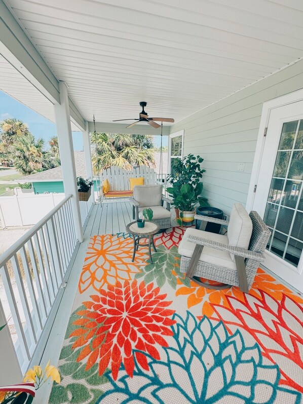 Un porche cubierto con un tapete de colores, muebles de mimbre y plantas en macetas.