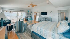 Un dormitorio amplio con una cama grande, ventilador de techo, televisor y vistas al exterior.