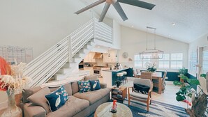 Una sala de estar amplia con un ventilador de techo alto, una escalera, una cocina y un comedor.
