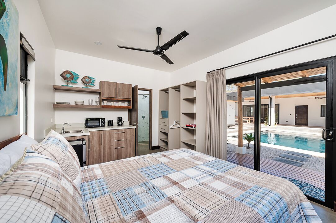 Ein Schlafzimmer mit Bett, einer Küchenzeile und einer Schiebetür zu einem Poolbereich.