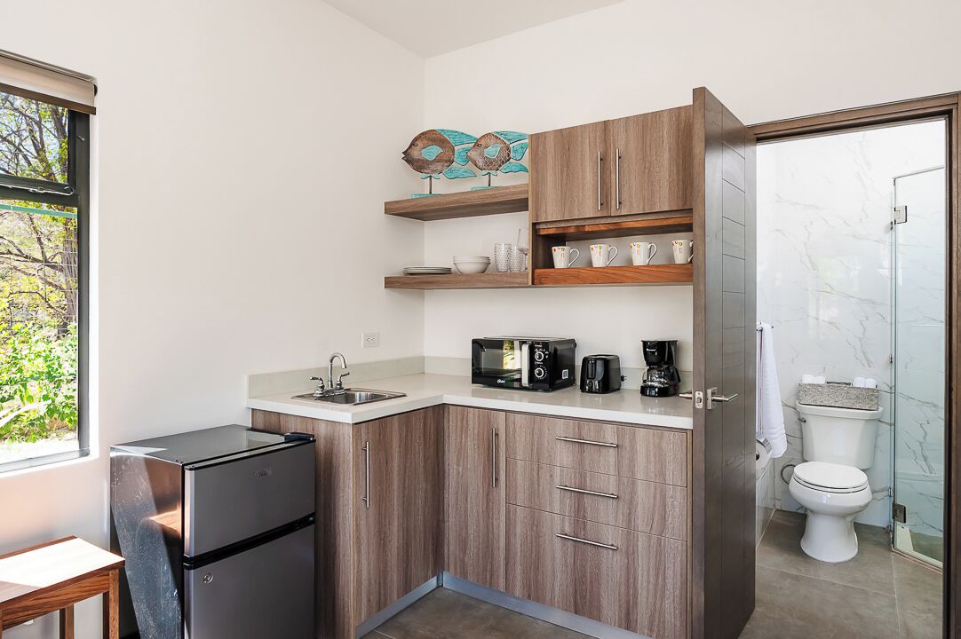 Una cucina funzionale con frigorifero, microonde, tostapane e macchina del caffè. Si notano pensili in legno e una parete rivestita in marmo.