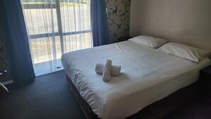 A hotel room with a large bed, a window with curtains, and a view of a parking area.
