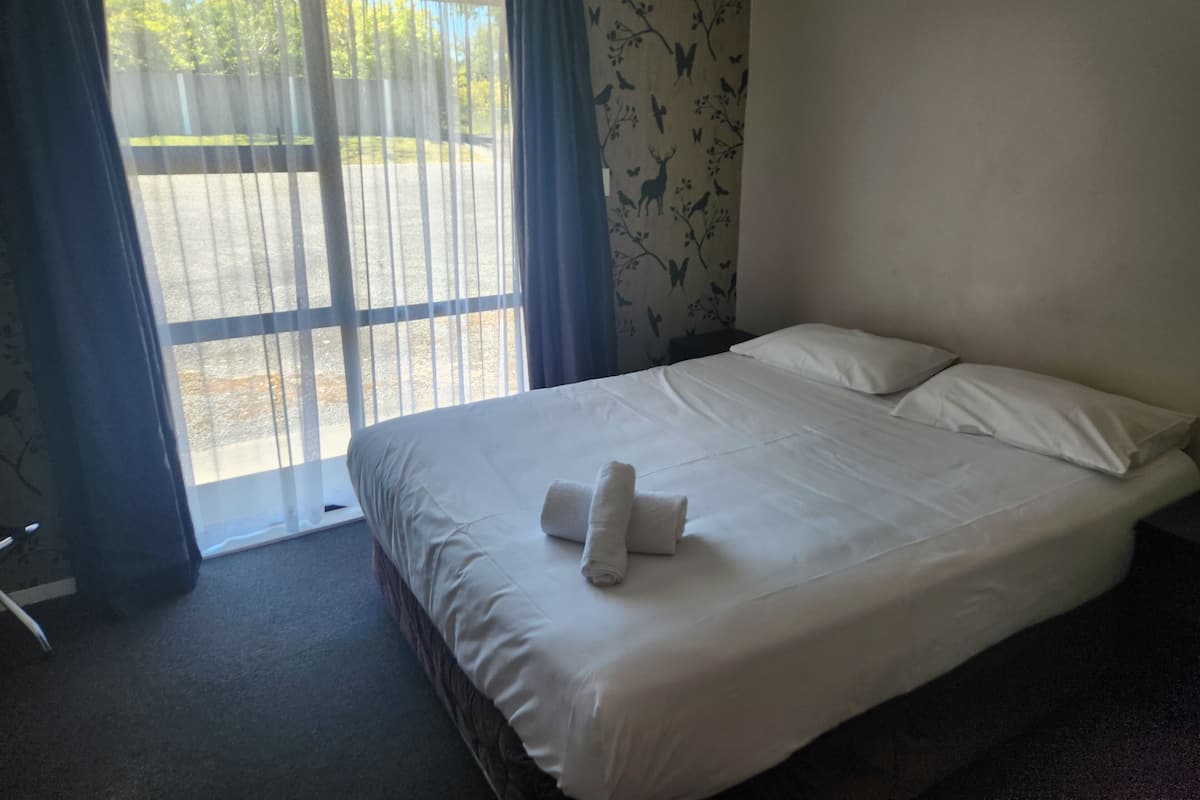Quarto de hotel com uma cama grande, janela com cortinas e vista para um estacionamento.