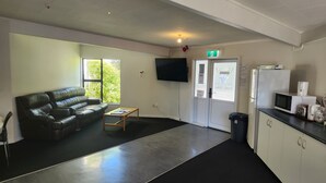 A room with a black leather sofa, a wooden coffee table, a flat-screen TV mounted on the wall, a refrigerator, and a microwave on the counter.