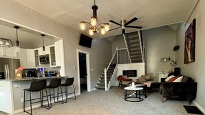 A modern kitchen with bar stools, a dining area with a round table, a staircase, and a living room with a sofa. - Charming 3-bedroom house with WiFi, AC in serene Noblesville (Noblesville)