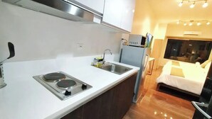 Una cucina moderna con piano cottura, lavello e frigorifero. Si nota un letto con copripiumino bianco e una finestra con tende.