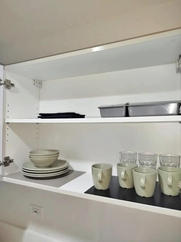 A kitchen with white cabinets, a black countertop, and a shelf with plates and cups.