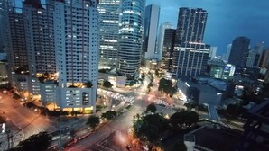 Paesaggio urbano al crepuscolo con grattacieli, un incrocio trafficato e strade illuminate.