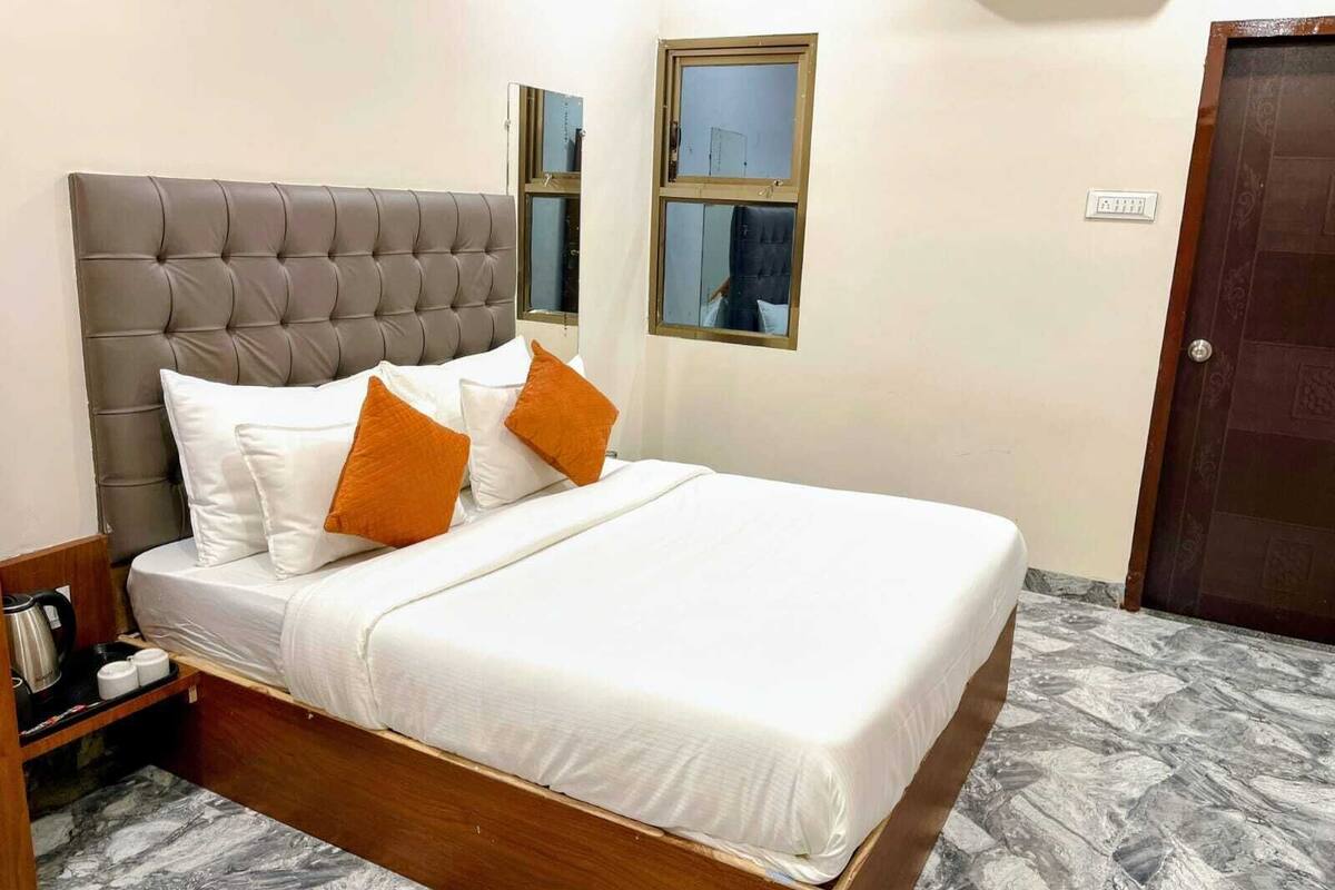A neatly made bed with white and orange pillows, a wooden headboard, and a marble-patterned floor.