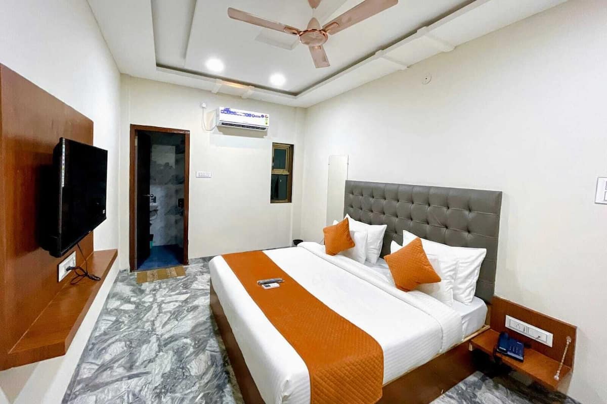 A hotel room with a bed, a television, a ceiling fan, and an air conditioning unit.