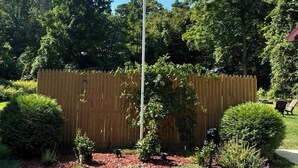 Un mât sur lequel flotte le drapeau américain, entouré d’une clôture en bois, d’un petit arbuste et d’une pelouse.