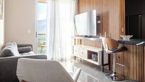 A modern hotel room with a sofa, a dining area with a bar, a TV, and a view of the city. - Departamento Punta Cero, Cintermex (Monterrey)