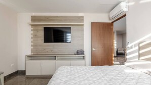 A bedroom with a bed, a built-in TV, a wardrobe, and a bathroom visible through an open door. - Departamento Punta Cero, Cintermex (Monterrey)