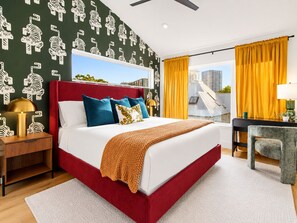 A modern hotel room with a red headboard, a large bed with multiple pillows, a view of the cityscape through a large window, and a desk with a lamp. - Downtown Austin Luxury Stay ★ Hot Tub • Fire Pit • Minigolf (Austin)