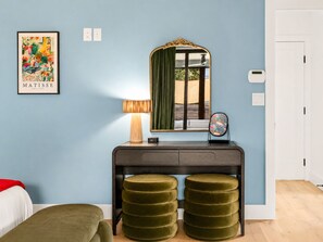 A room with a blue wall, a framed artwork, a desk with a mirror, a lamp, and two ottomans. - Downtown Austin Luxury Stay ★ Hot Tub • Fire Pit • Minigolf (Austin)