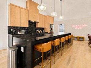 A modern kitchen with a black countertop, wooden cabinets, and a bar area with stools. - Downtown Austin Luxury Stay ★ Hot Tub • Fire Pit • Minigolf (Austin)
