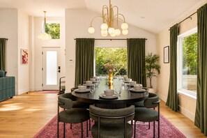 A dining area with a round table set for six, surrounded by six chairs, a chandelier, and a view of greenery outside. - Downtown Austin Luxury Stay ★ Hot Tub • Fire Pit • Minigolf (Austin)