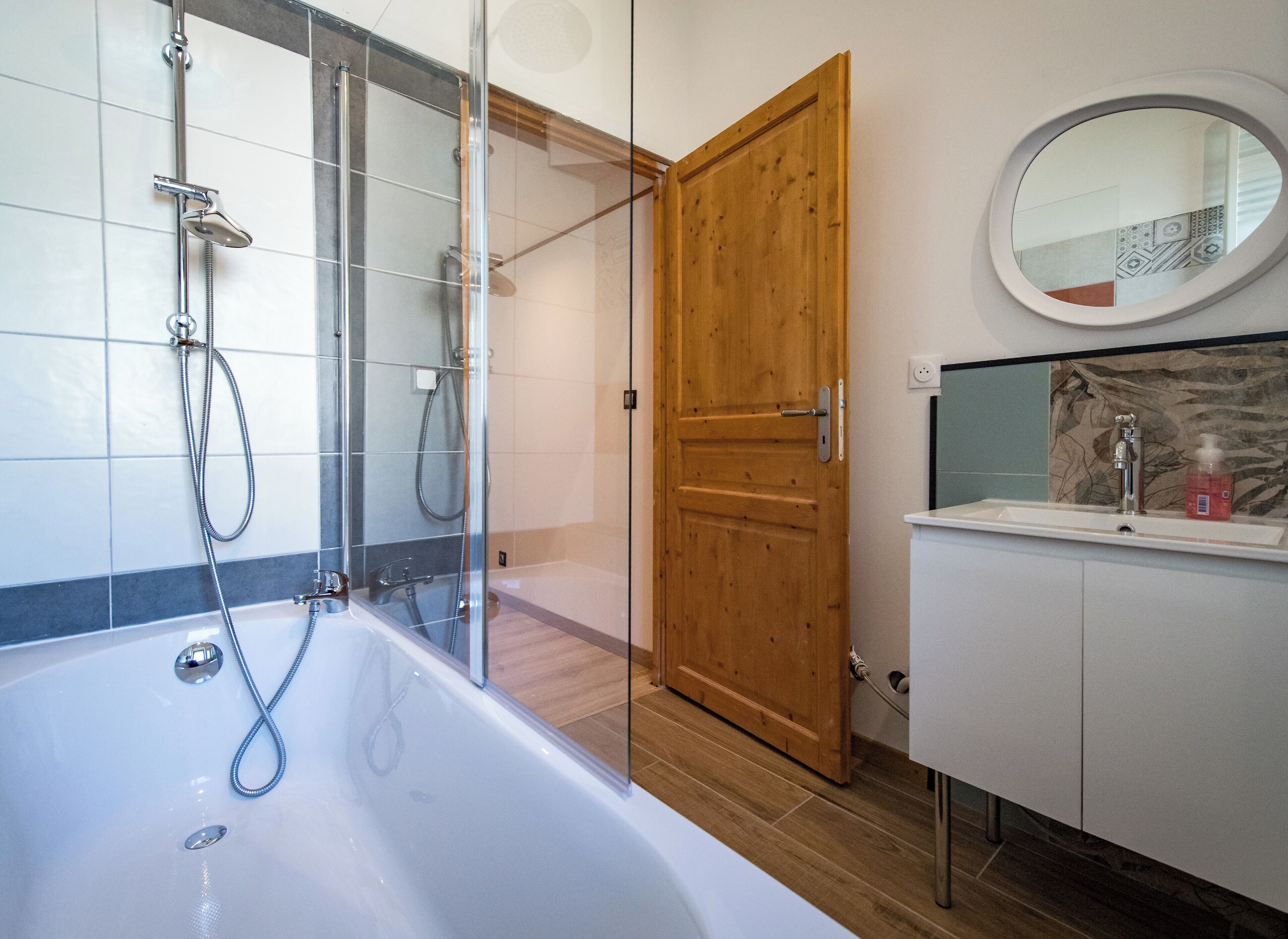 A modern bathroom with a glass-enclosed shower, a wooden door, and a white vanity with a mirror.