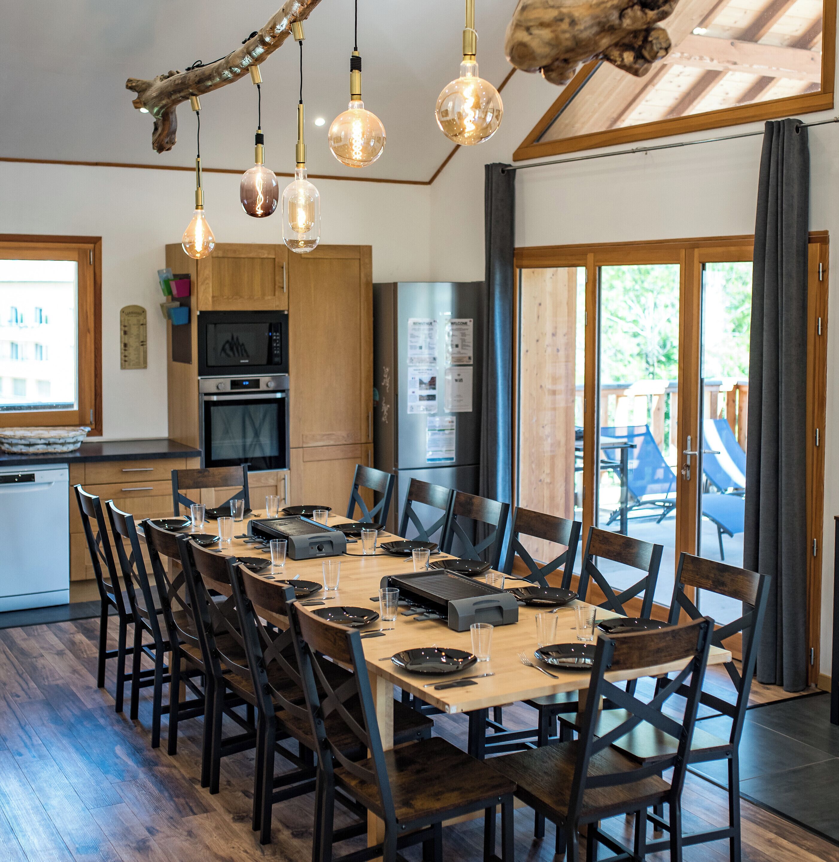Un comedor moderno con una mesa de madera larga, sillas negras y lámparas colgantes.