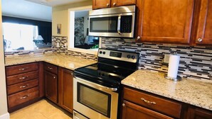 A kitchen with wooden cabinets, a stainless steel stove, a microwave, and a tiled backsplash. - Awesome Condo in Acme, Michigan (Williamsburg)