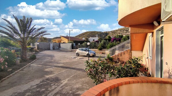 A residential area with a paved driveway, a parked car, and a building with a balcony.